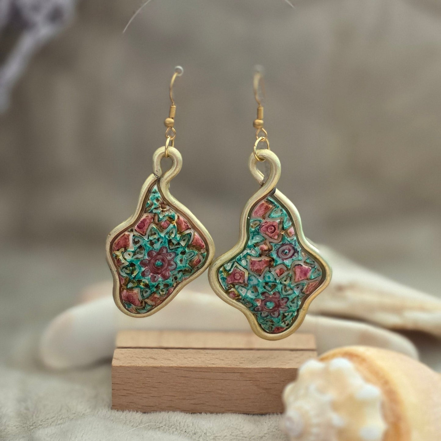 Aretes artesanales en polymer clay con diseño floral en tonos verdes y rosados, enmarcados en alambre. Joyería única, ligera y elegante de la colección Singular.