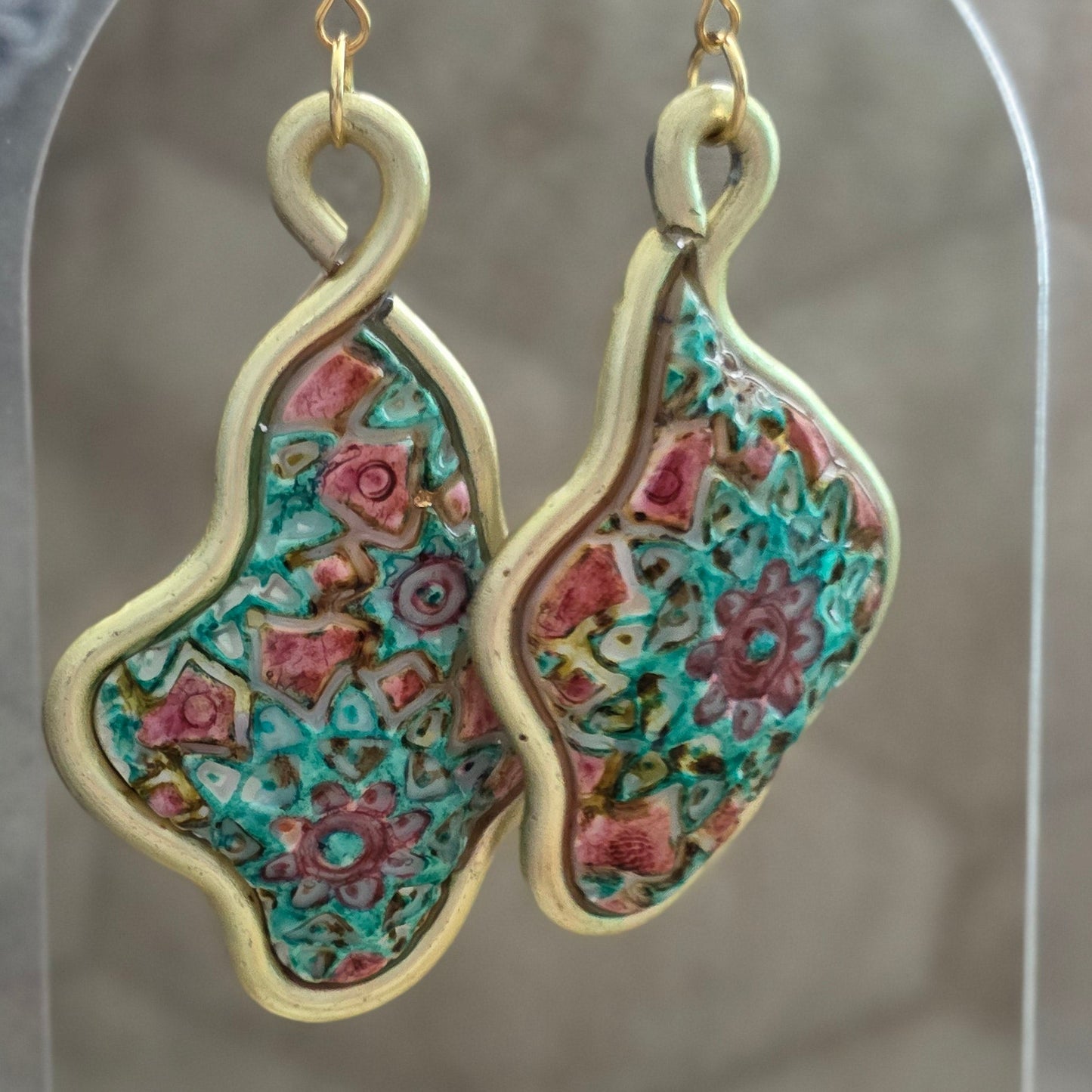 Aretes artesanales en polymer clay con diseño floral en tonos verdes y rosados, enmarcados en alambre. Joyería única, ligera y elegante de la colección Singular.