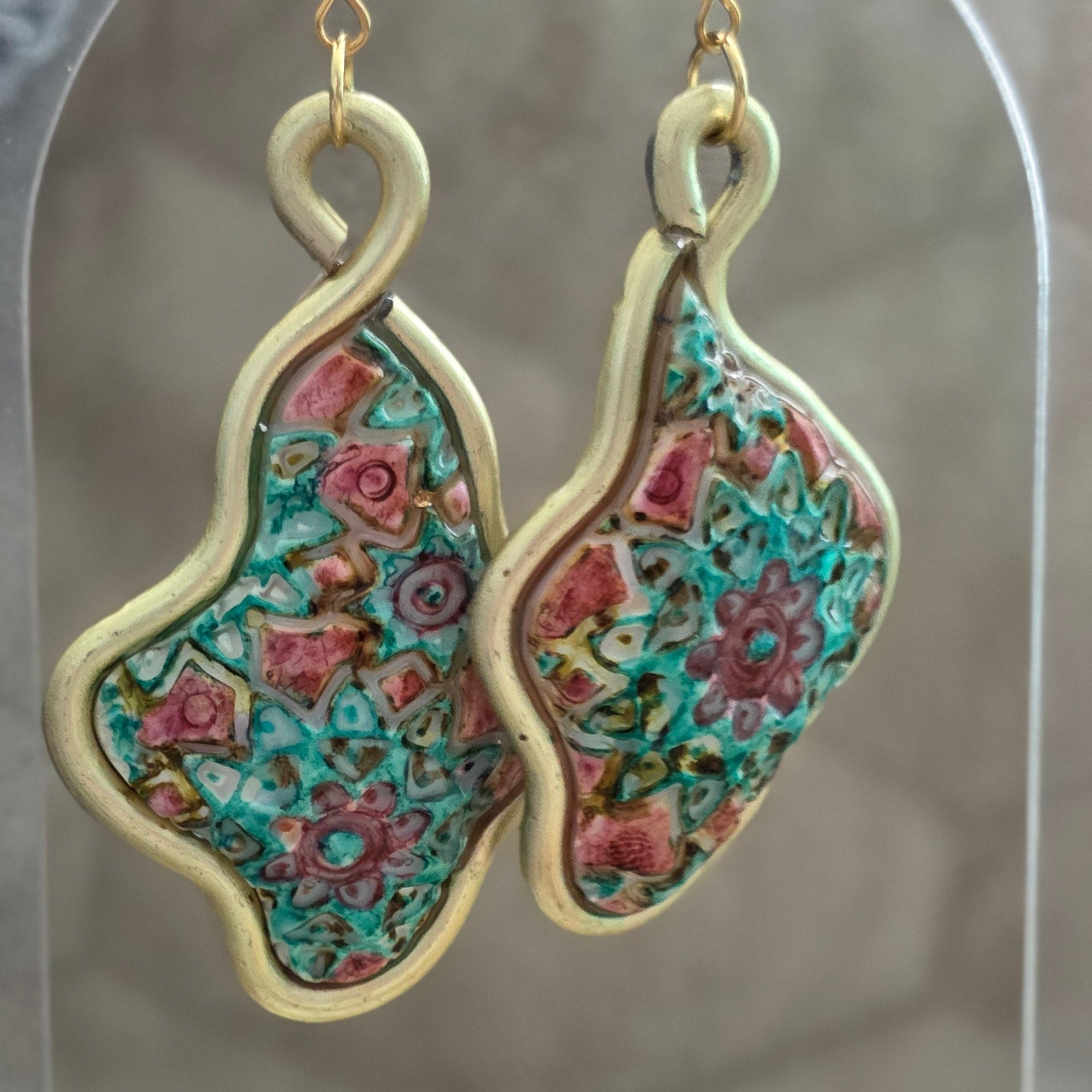 Aretes artesanales en polymer clay con diseño floral en tonos verdes y rosados, enmarcados en alambre. Joyería única, ligera y elegante de la colección Singular.