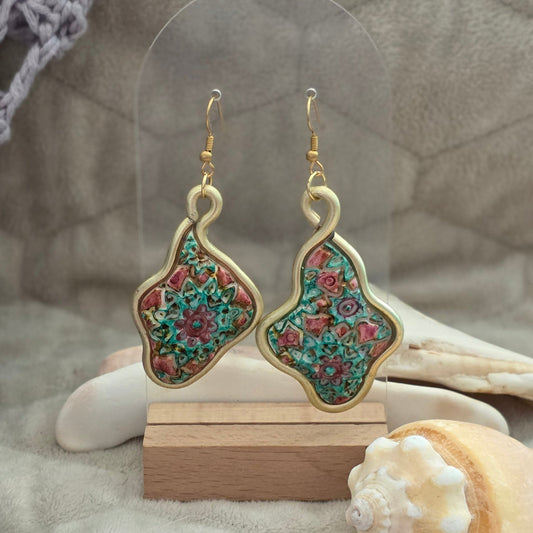 Aretes artesanales en polymer clay con diseño floral en tonos verdes y rosados, enmarcados en alambre. Joyería única, ligera y elegante de la colección Singular.