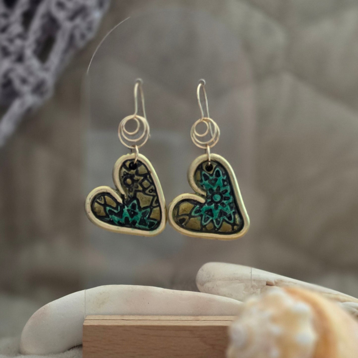 Heart-shaped earrings with gemstones held by a gloved hand against a neutral background
