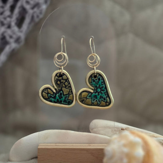 Heart-shaped earrings with gemstones held by a gloved hand against a neutral background