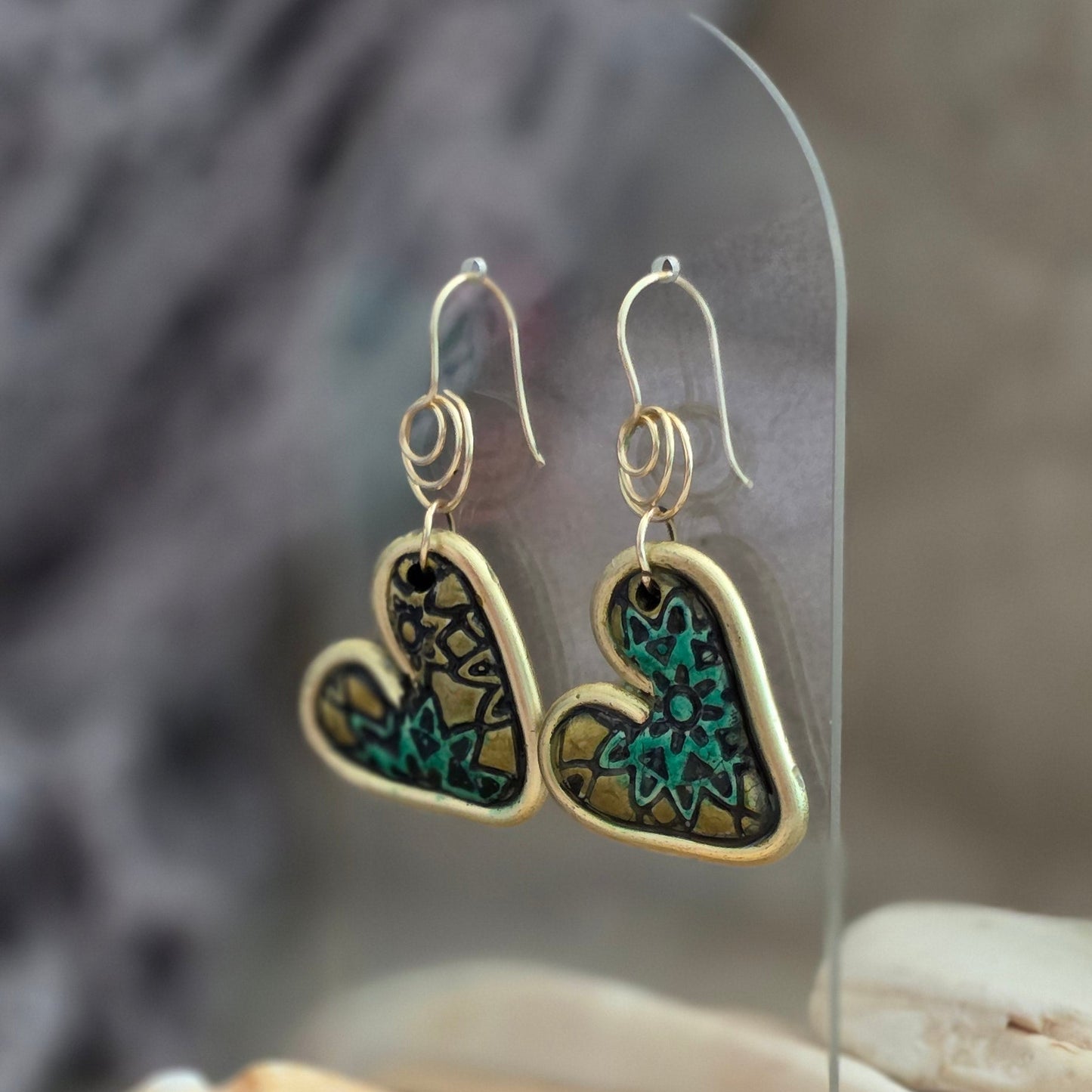 Heart-shaped earrings with gold and blue design on a reflective surface with seashells.