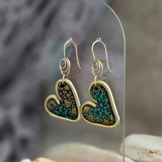 Heart-shaped earrings with gold and blue design on a reflective surface with seashells.