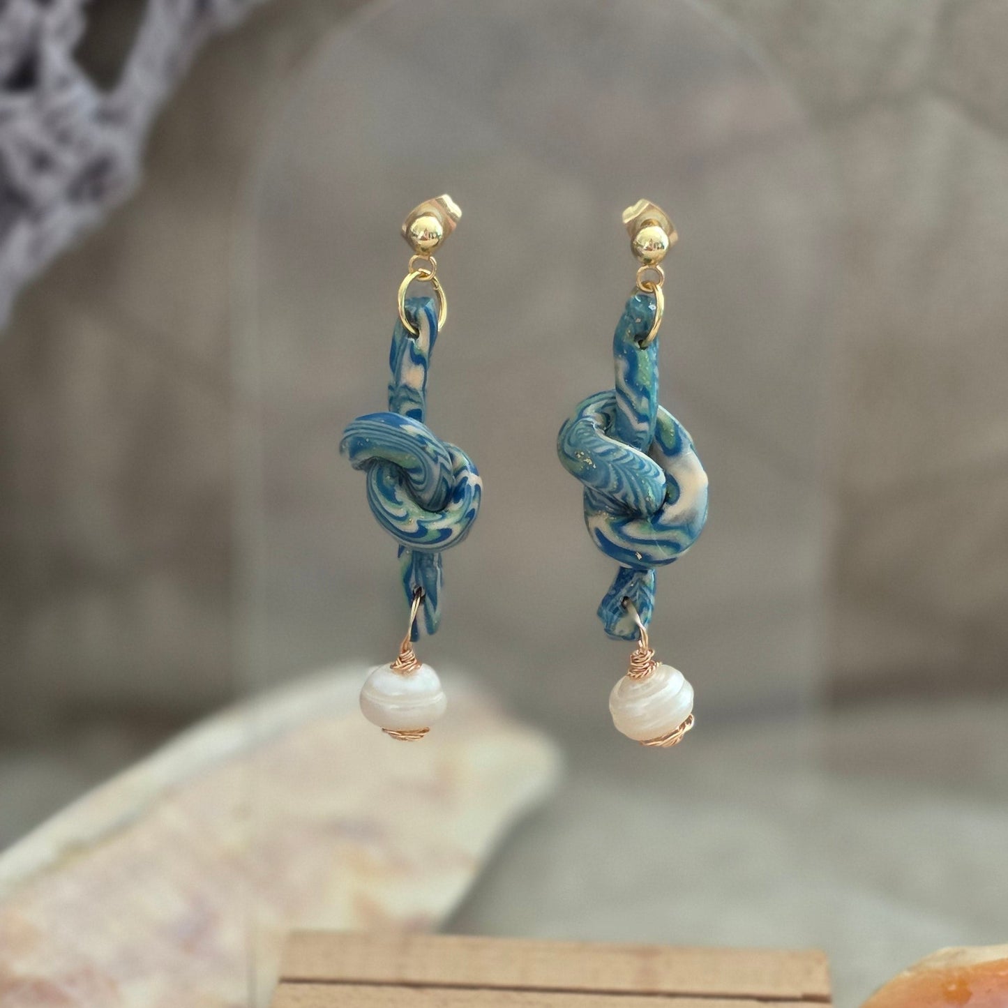 Aretes hechos a mano en polymer clay marmolizado con diseño de nudo y perla natural. Joyería única, elegante y ligera de la colección Singular.