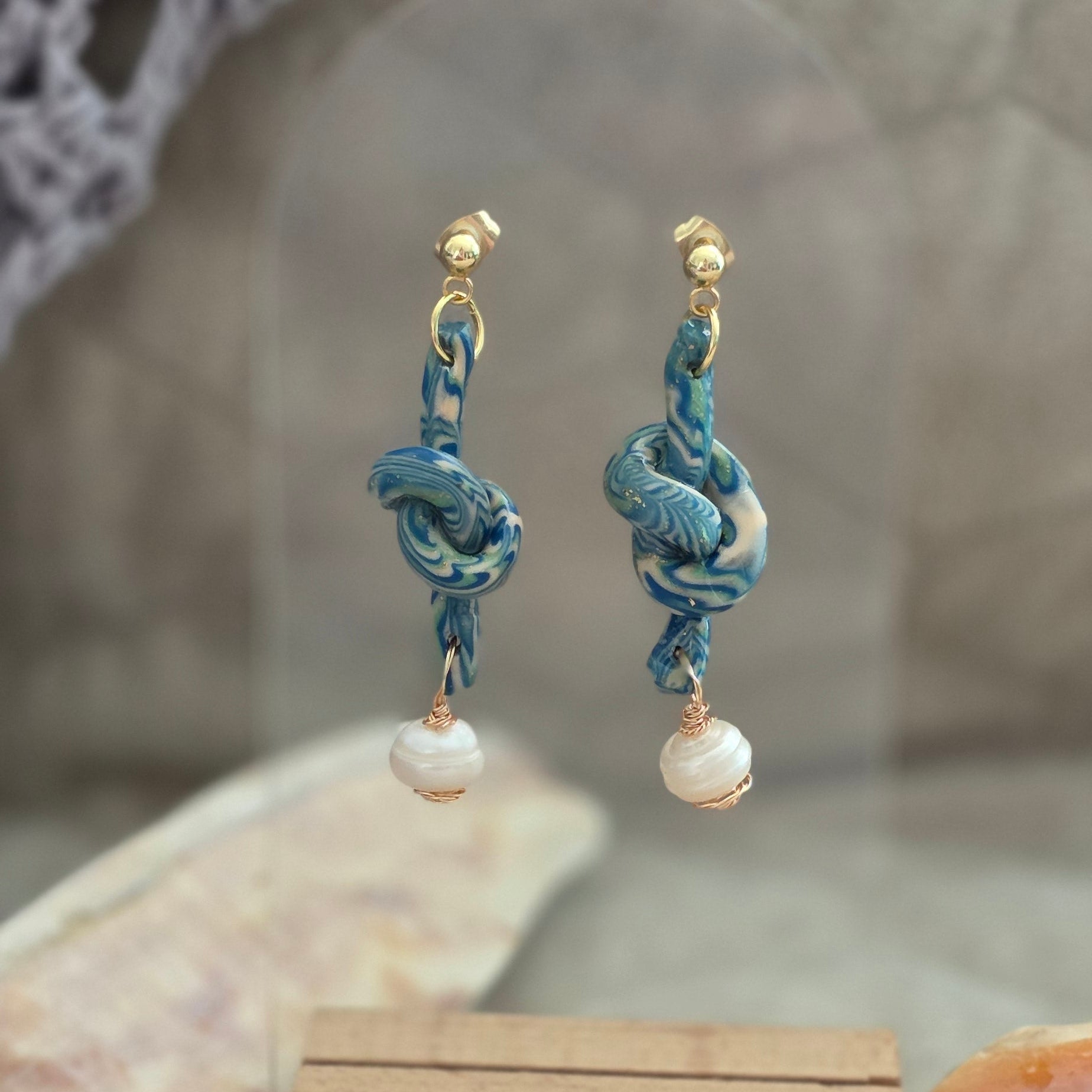 Aretes hechos a mano en polymer clay marmolizado con diseño de nudo y perla natural. Joyería única, elegante y ligera de la colección Singular.