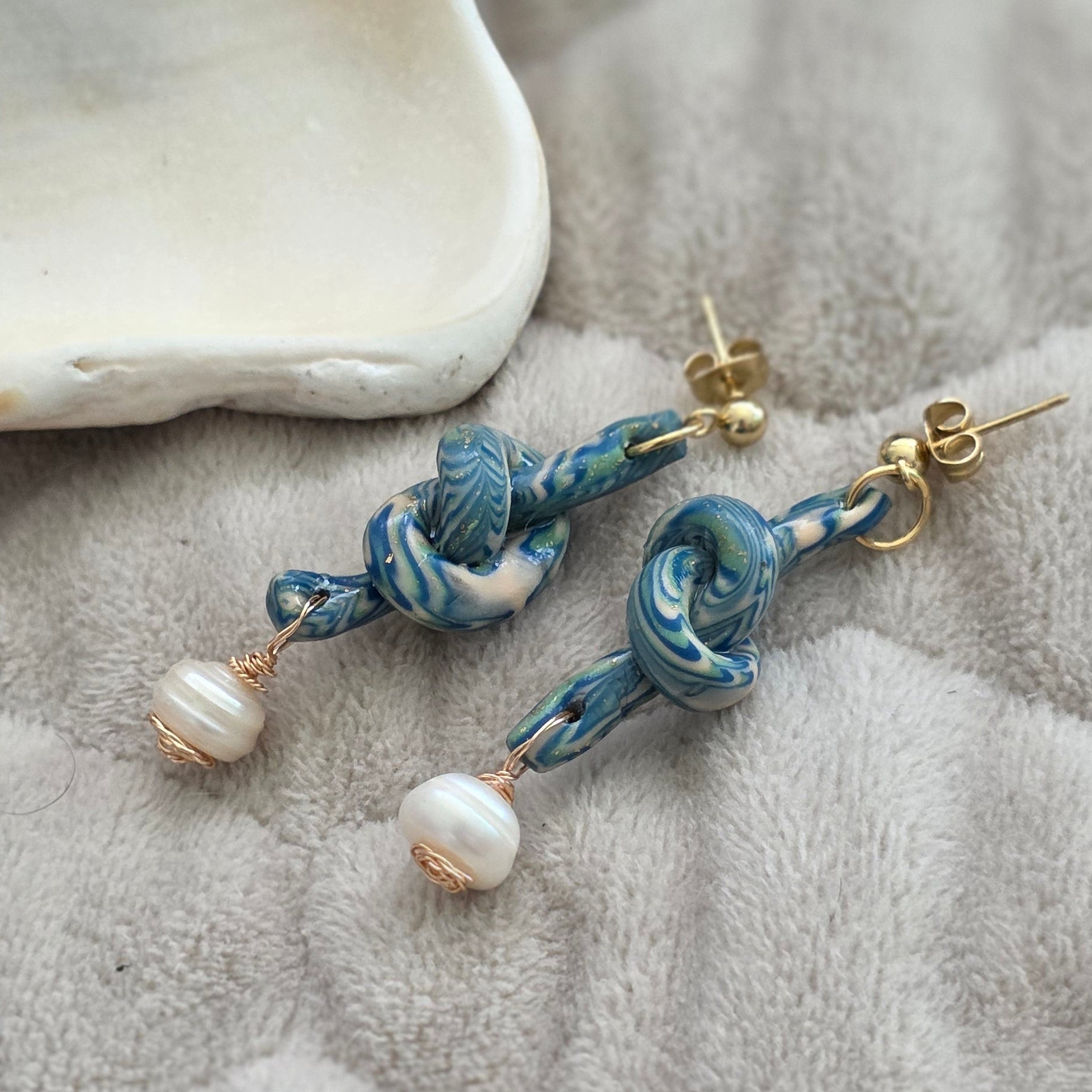 Aretes hechos a mano en polymer clay marmolizado con diseño de nudo y perla natural. Joyería única, elegante y ligera de la colección Singular.