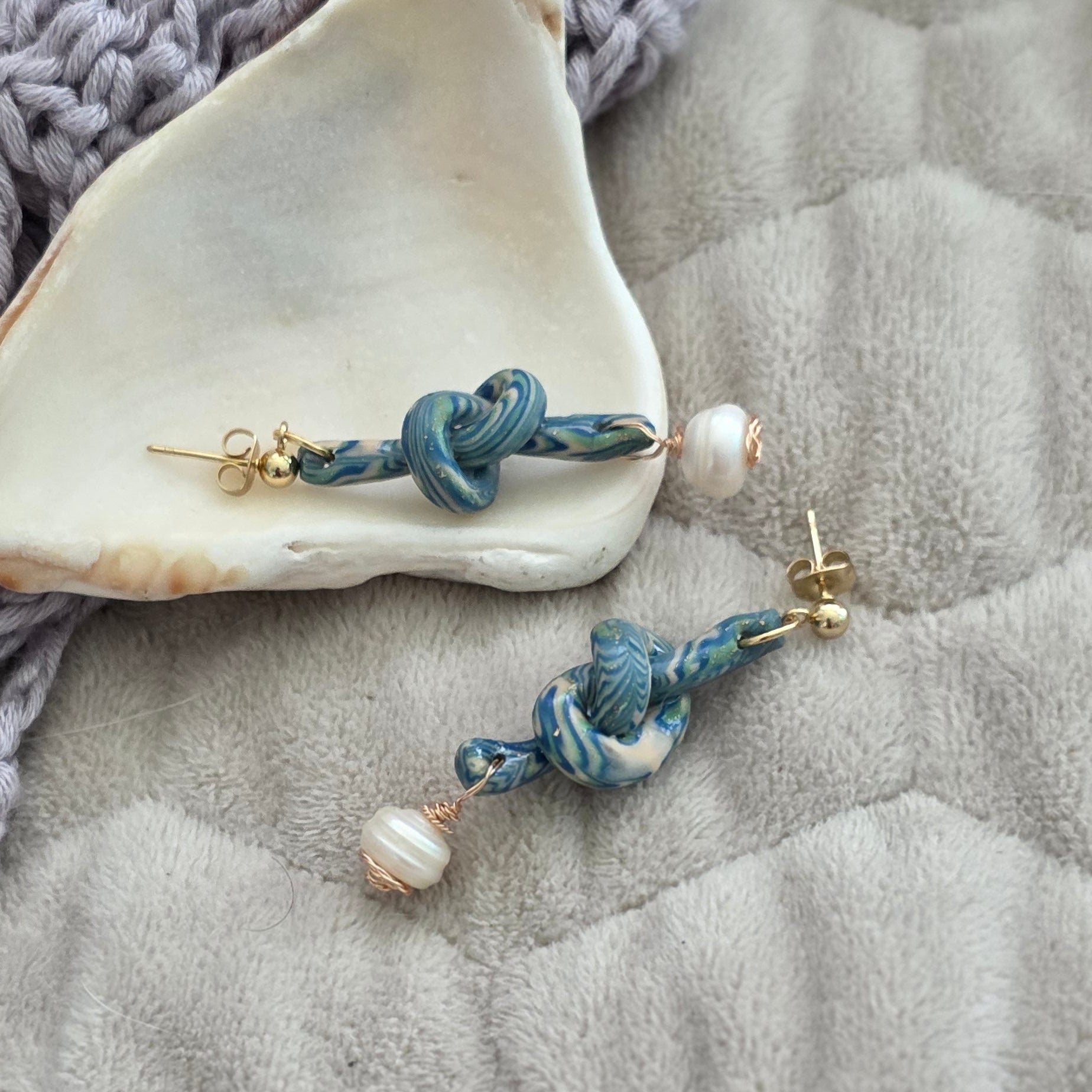 Aretes hechos a mano en polymer clay marmolizado con diseño de nudo y perla natural. Joyería única, elegante y ligera de la colección Singular.