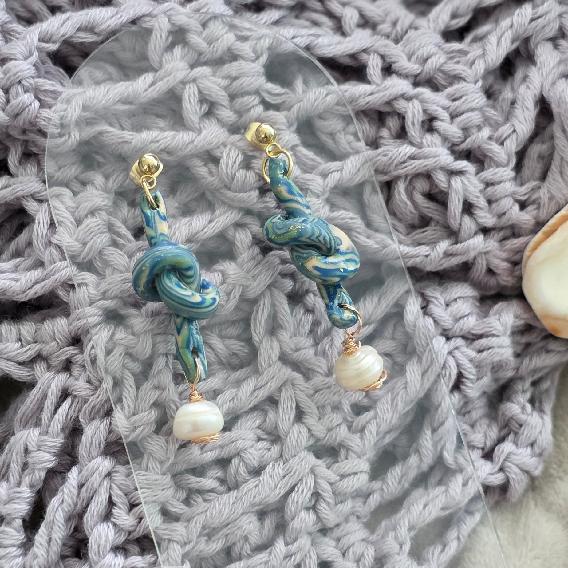Aretes hechos a mano en polymer clay marmolizado con diseño de nudo y perla natural. Joyería única, elegante y ligera de la colección Singular.