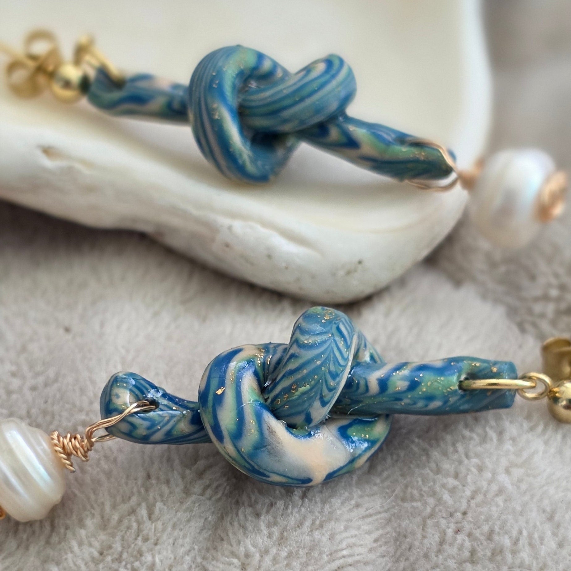 Aretes hechos a mano en polymer clay marmolizado con diseño de nudo y perla natural. Joyería única, elegante y ligera de la colección Singular.